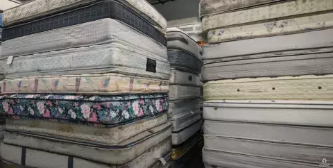 Palettes sit in a warehouse stacked high with used mattresses.